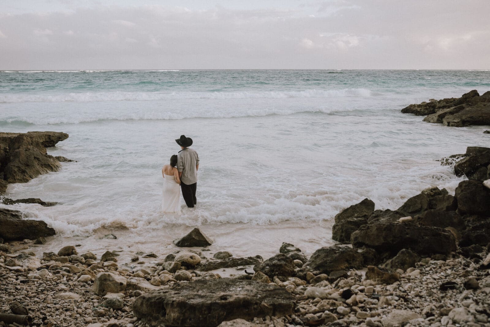 Intimate beach elopement in Tulum as a couple stands barefoot in the waves at sunset