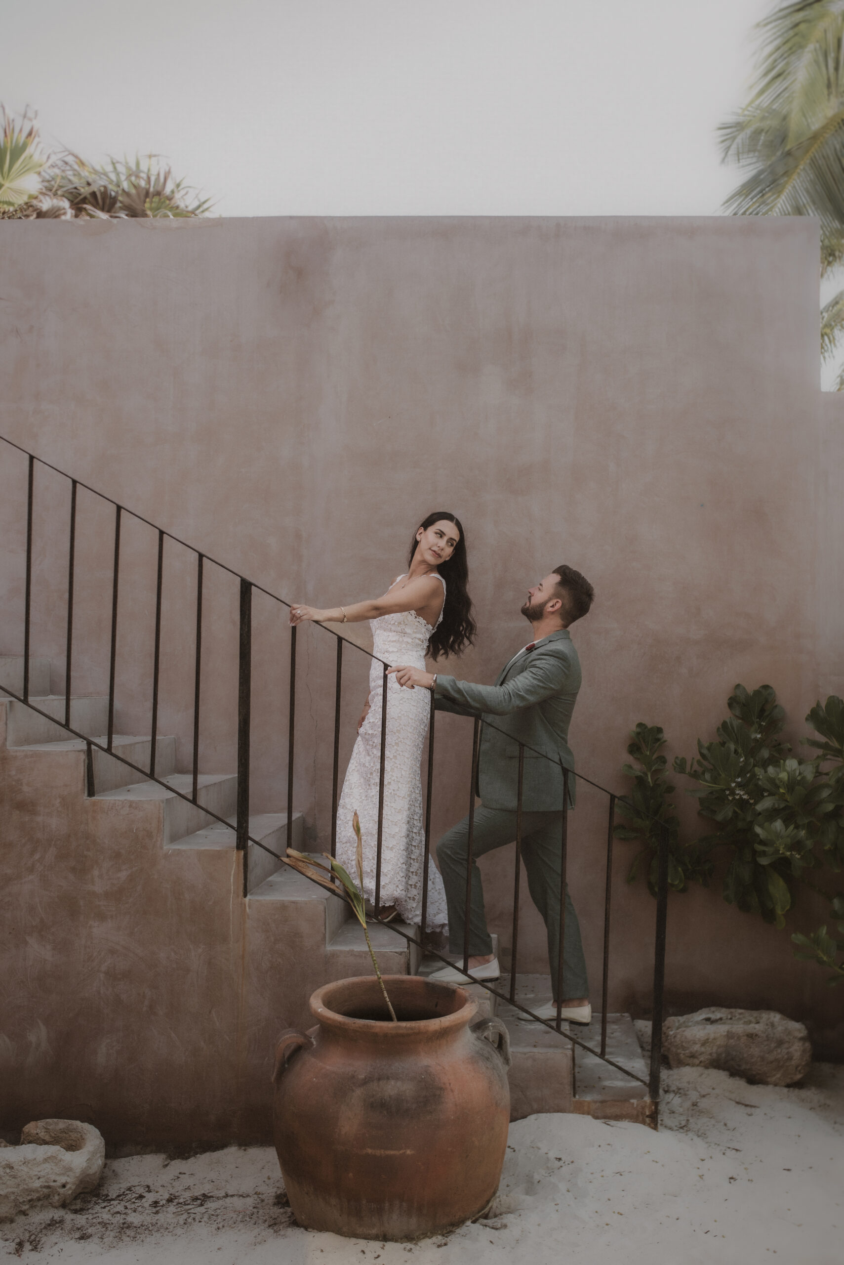 Bride and groom walk up the stairs against the mauve chukum backdrop of Xela Tulum before their elopement ceremony.