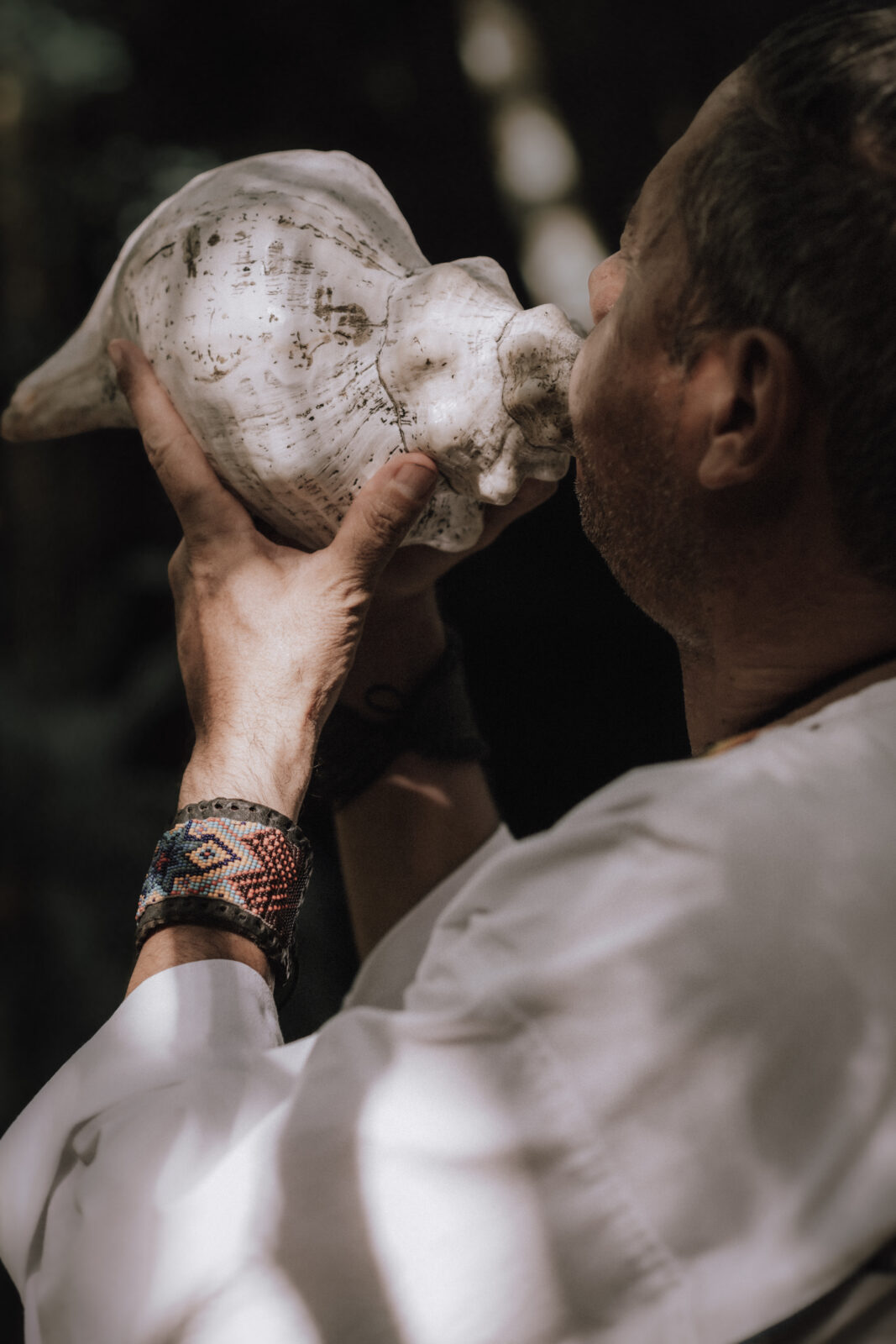 Mayan Shaman blows into conch during a Mayan Elopement Ceremony at a cenote in Tulum, Mexico.