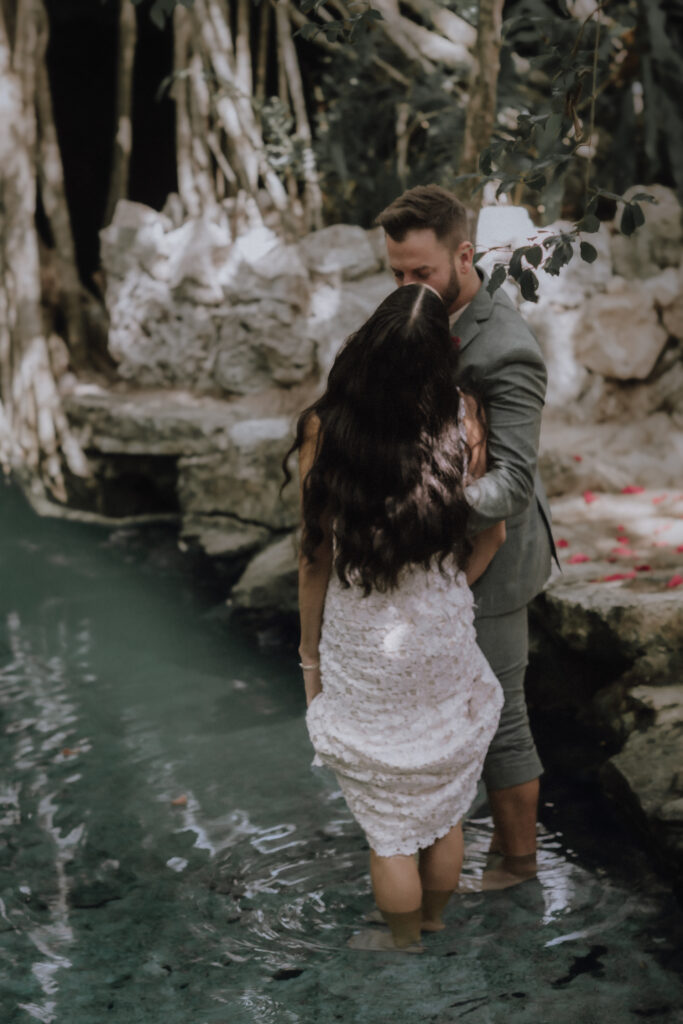After their Mayan elopement ceremony the bride and groom stand in the refreshing water of the cenote in Tulum.